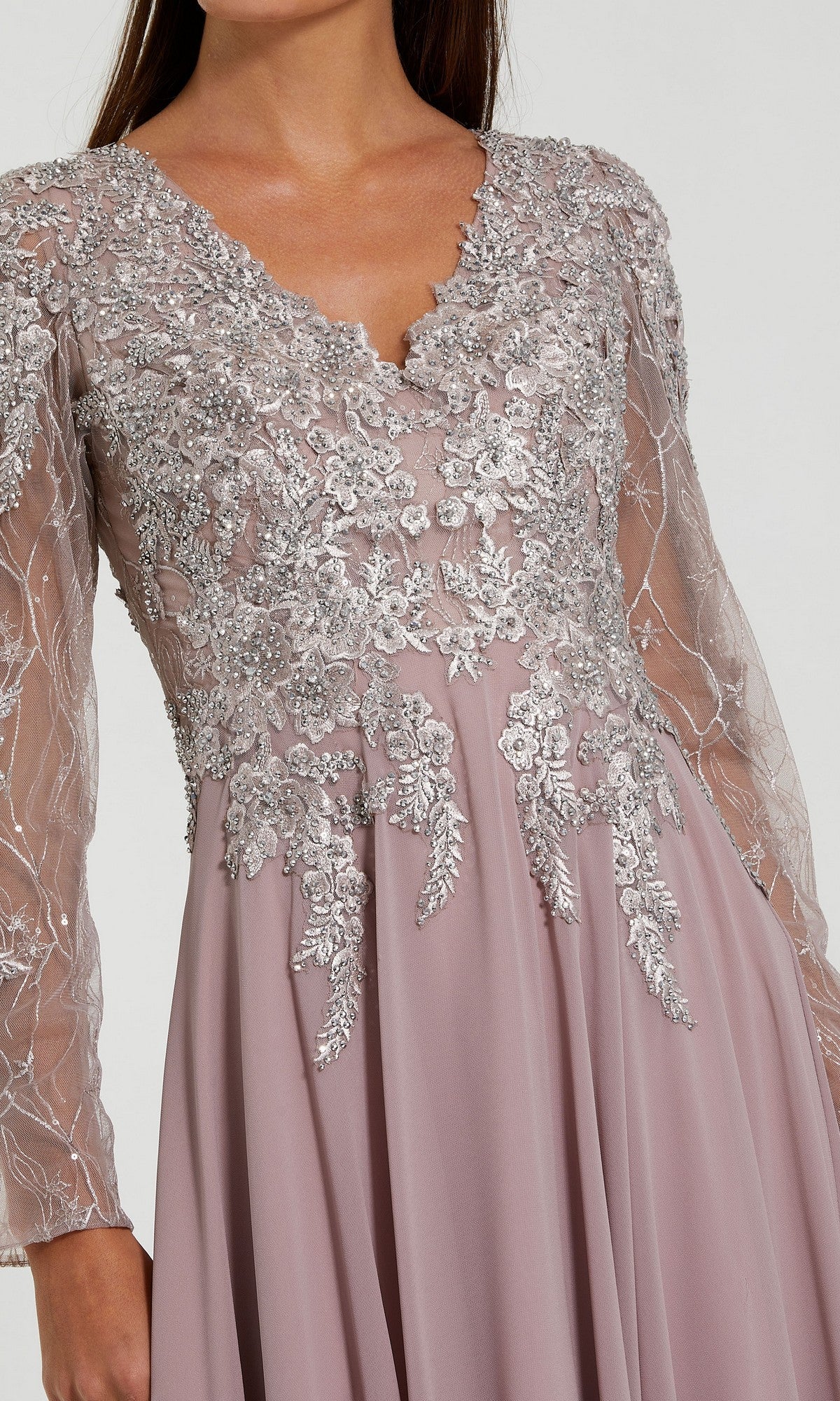 A woman wears the Mac Duggal 20388, a mauve chiffon long sleeve special occasion dress with sheer sleeves and silver floral embroidery on the bodice and sleeves.
